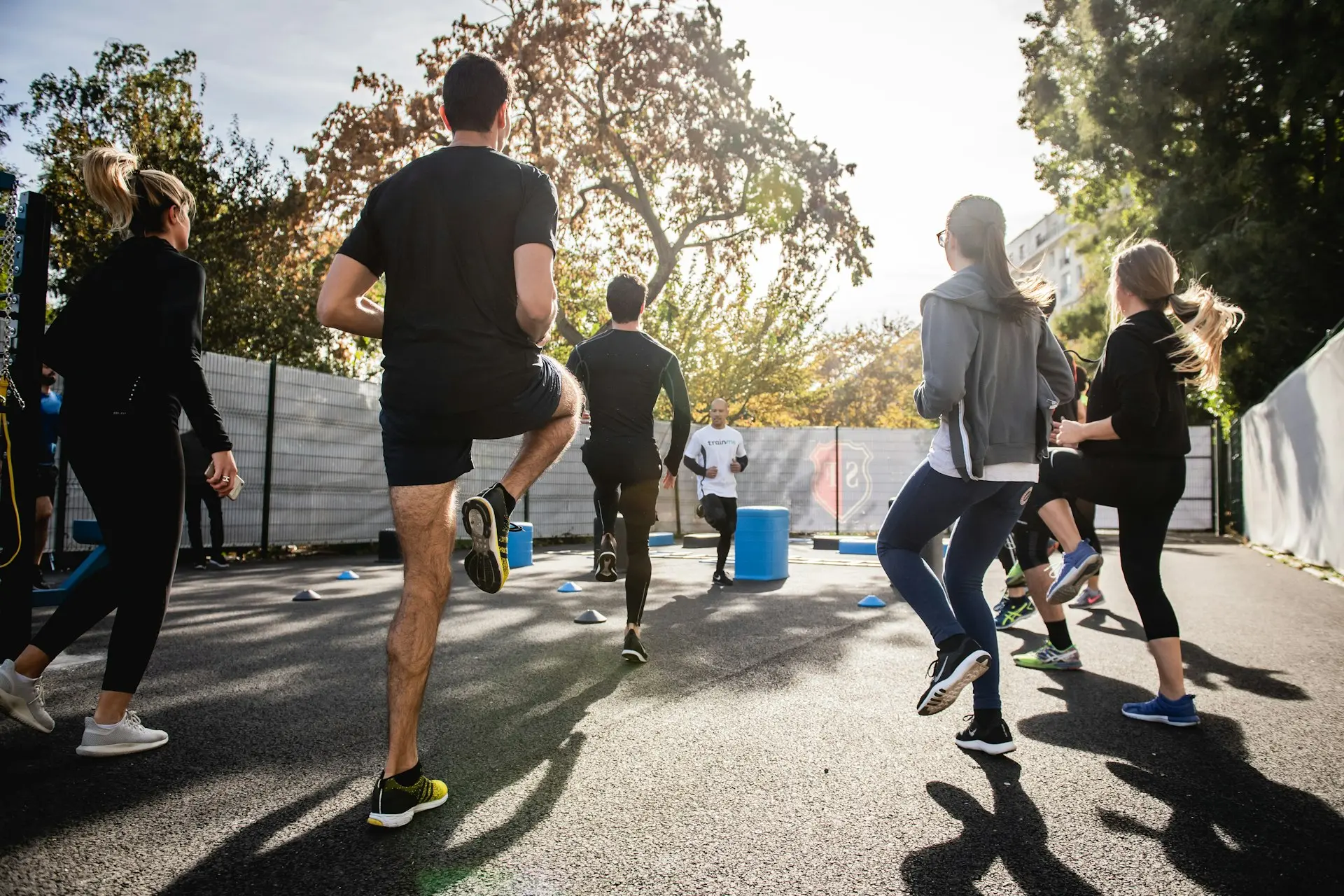Mobilité, activation et préparation : les clés d’un bon échauffement. Un groupe de personnes réalisant des exercices d’échauffement sous la direction d’un coach, avec des montées de genoux et des talons-fesses.