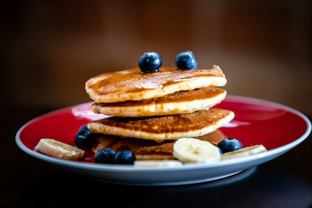 Assiette de pancakes garnis de bananes et de myrtilles, illustrant une alimentation saine et nutritive pour l’énergie et la récupération.