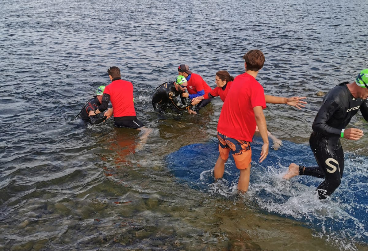 Sortie de l’eau après l’épreuve de natation de 3800m, aidé par les bénévoles. Encore en combinaison de nage, les premiers instants de transition débutent.