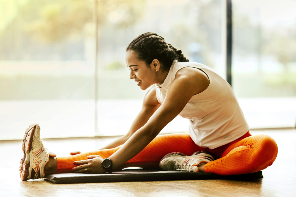 Prendre soin de son corps : l’importance des étirements pour une meilleure récupération. Femme en tenue de sport réalisant des étirements avec le sourire, soulignant l’importance de la souplesse, de la récupération et du bien-être après l’effort.